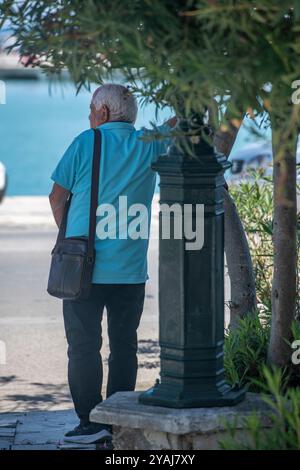 Vieux gentleman ombrage du soleil d'été chaud sous un arbre au bord de la route en Grèce. Banque D'Images