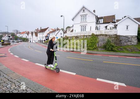 Stavanger, Norvège - 6 août 2022 : femme conduit un scooter électrique au bord d'une route à Stavanger, Norvège, près du quartier historique de Gamle St. Banque D'Images