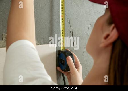 Femme carrelant les murs de salle de bains, en utilisant le mètre ruban pour mesurer la longueur. Processus d'installation de carreaux dans la salle de bain étape par étape. Bricolage maison Improvem Banque D'Images