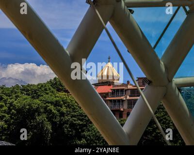 le dôme doré et la croix de la cathédrale sameba de la trinité sainte sont encadrés par la charpente en acier de l'emblématique pont de la paix od tbilissi géorgie Banque D'Images