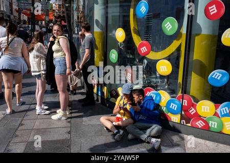 Touristes et visiteurs nationaux dans le West End à Leicester Square devant le magasin M&MS le 28 juillet 2024 à Londres, Royaume-Uni. Londres est l’une des principales destinations touristiques au monde et joue un rôle vital dans le secteur touristique du Royaume-Uni. La ville attire des millions de visiteurs internationaux ainsi que des touristes nationaux et des voyageurs d'une journée chaque année, et par conséquent, certains quartiers du centre de Londres regorgent de gens aux périodes de forte activité de l'année. Le secteur des voyages et du tourisme au Royaume-Uni contribue grandement à l'économie, le secteur du tourisme employant quelque 700 000 personnes. Banque D'Images