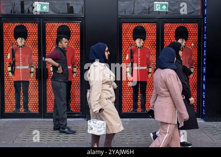 Des gens de passage interagissent avec CUT of a Grenadier Guardsman en uniforme militaire complet devant un magasin de souvenirs et de bagages sur Oxford Street le 7 octobre 2024 à Londres, au Royaume-Uni. Londres est l'une des principales destinations touristiques du monde, avec de nombreuses attractions touristiques célèbres. La ville attire des millions de visiteurs internationaux ainsi que des touristes nationaux et des voyageurs d'une journée chaque année. Le secteur des voyages et du tourisme au Royaume-Uni contribue grandement à l'économie, le secteur du tourisme employant quelque 700 000 personnes. Banque D'Images