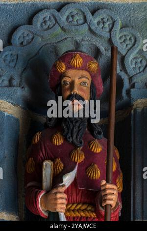 Saint Jacques l'Apôtre, fils de Zébédée, ses vêtements ornés de coquilles de coques ou de coquilles Saint-Jacques et tenant le bâton d'un pèlerin. Statue peinte sculptée en bois en 1721 et l’une des 12 statues apôtres flanquant l’entrée d’une église bretonne, L’Eglise Saint Sauveur au Faou, Finistère, Bretagne, France. Banque D'Images