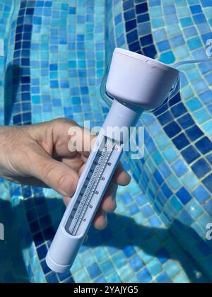 Personne vérifiant la température de l'eau dans la piscine à l'aide d'un thermomètre Banque D'Images