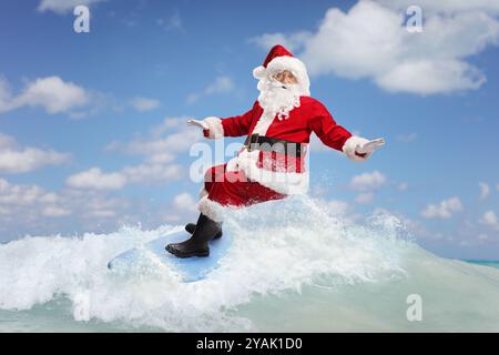 Père noël chevauchant une planche de surf sur une vague dans la mer Banque D'Images