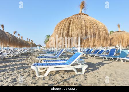 Rangée de chaises longues bleues et blanches avec parasols de paille sur le sable d'une plage à Torremolinos, Malaga, Andalousie, Espagne Banque D'Images