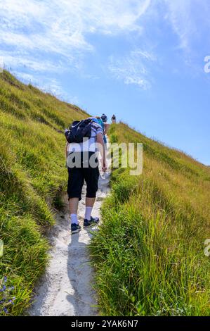 Un groupe de personnes emprunte le sentier de craie très escarpé jusqu'à Haven Brow, le premier sommet des Seven Sisters dans le Sussex de l'est, en Angleterre. Banque D'Images