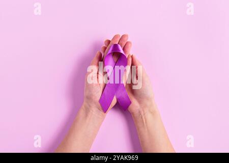 Ruban de cancer violet dans les mains des femmes sur fond rose Banque D'Images