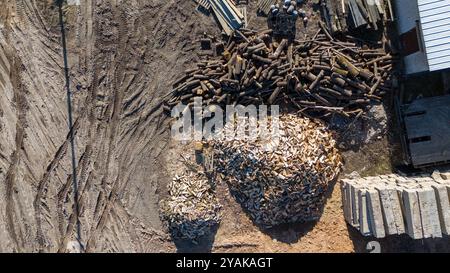 Vue aérienne d'une cour de bois montrant des piles de billes et de pieux de bois sur une surface de terre. La scène comprend différentes tailles de bois, certains soigneusement empilés Banque D'Images