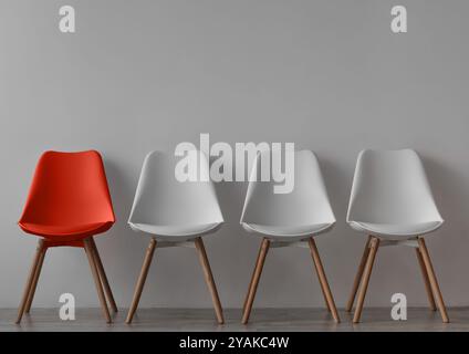 Trois chaises blanches vacantes et une rouge sur fond de mur gris dans le bureau ou la chambre Banque D'Images