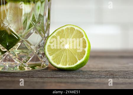 Gros plan d'un citron vert coupé en deux à côté d'un cocktail de caipirinha sur une table en bois. tuiles blanches en arrière-plan. Banque D'Images