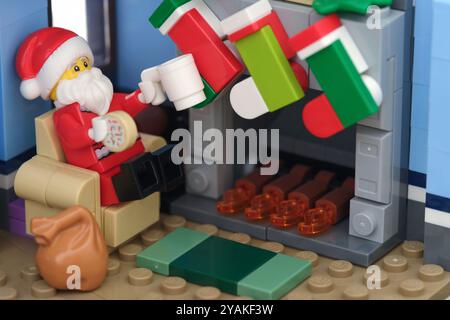 Tambov, Fédération de Russie - 14 octobre 2024 Une figurine Lego Santa Claus assise dans un fauteuil, mangeant un biscuit et buvant du lait près d'une cheminée Banque D'Images