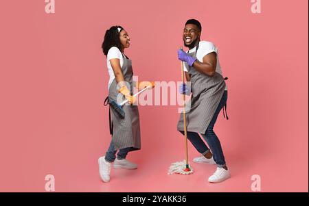 Concept de service d'entretien joyeux. Couple africain joyeux de nettoyeurs ayant du plaisir pendant les tâches Banque D'Images