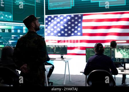 Homme militaire AMÉRICAIN supervisant l'activité de détection des menaces dans le bureau de haute technologie, examinant les données top secrètes sur grand écran. Soldats gouvernementaux gérant la guerre hybride, prévention des cyberattaques. Banque D'Images