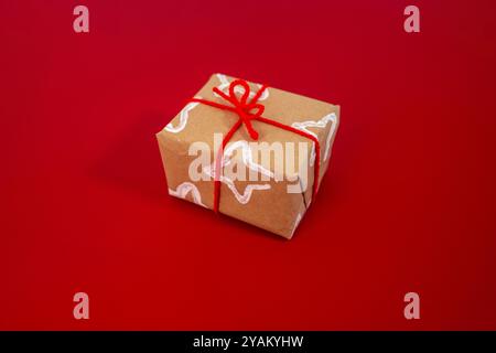 un cadeau enveloppé dans du papier brun orné d'un motif d'étoile blanche créé à l'aide d'un rouleau de papier toilette plié. Le cadeau est attaché avec un ruban rouge vif, dec Banque D'Images