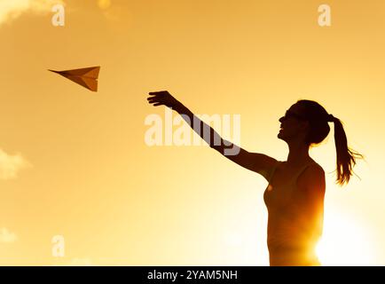 Prendre son envol ! Jeune femme jetant un avion de papier dans le ciel. Futur, vision, concept de direction. Banque D'Images