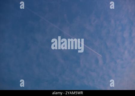 Avion volant à travers le ciel laissant une longue traînée de vapeur sur un fond de nuages bleu et rose doux pendant la soirée Banque D'Images