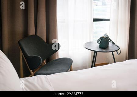 Chambre d'hôtel avec lit recouvert d'une couverture blanche, chaise et table. Banque D'Images