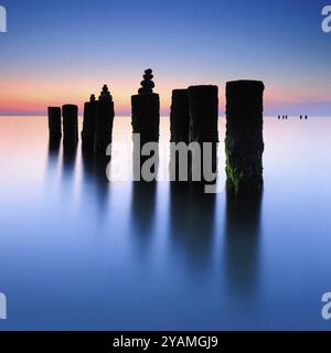 Pyramides de pierre sur les vieux groynes avec des algues dans l'eau sur la plage de la mer Baltique, longue exposition au coucher du soleil, Wustrow, Fischland-Darss-Zingst peninsu Banque D'Images