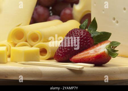 Un ensemble de différents fromages, fraises et raisins sur une planche de bois Banque D'Images