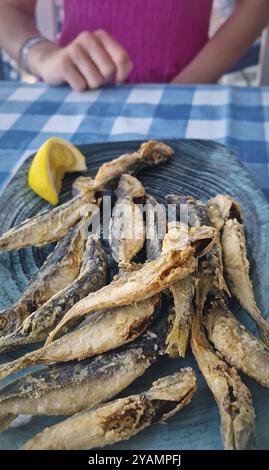 Gros plan assiette de poisson frit de maquereau cheval sur la table dans un restaurant et une femme pressant du jus de citron au-dessus, prêt à profiter du repas Banque D'Images