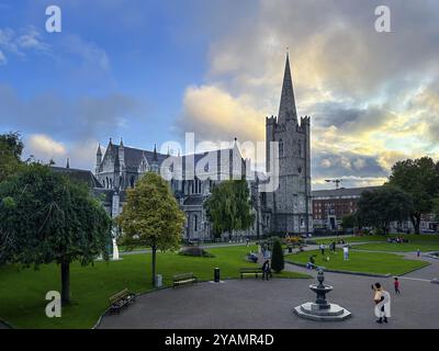 Cathédrale gothique entourée d'un parc verdoyant et d'arbres, sous un ciel légèrement nuageux avec des gens au premier plan, cathédrale St Patrick, Dublin, Irelan Banque D'Images