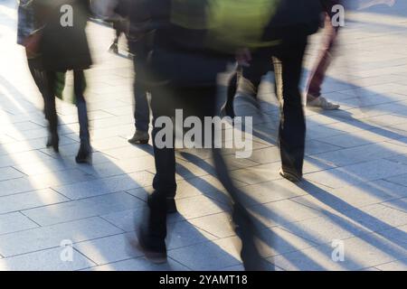 Les piétons se dirigent vers le soleil couchant, pour les jeter sur le trottoir de longues ombres. Image prise avec une longue exposition, mouvement flou Banque D'Images