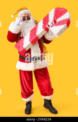 Cool Santa Claus avec pinata de canne à sucre sur fond jaune Banque D'Images