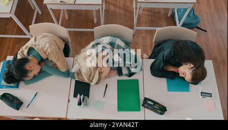 Fatigué, endormi et groupe d'élèves sur le bureau dans la salle de classe à l'école avec fatigue dans la leçon pour l'apprentissage. Burnout, repos et adolescents avec sieste pour Banque D'Images