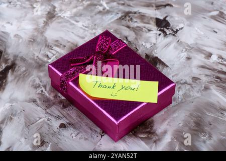 Un coffret cadeau violet éclatant orné d'une note disant Merci sur un fond artistique Banque D'Images