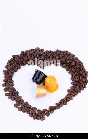 Un cœur artistique fait de grains de café, avec des capsules de café au milieu, magnifiquement affichées sur une surface blanche Banque D'Images