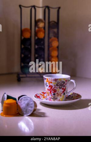 Une tasse de café fraîchement préparé à la vapeur se trouve à côté des capsules de café et d'un support, créant une atmosphère chaleureuse idéale pour les amateurs de café Banque D'Images