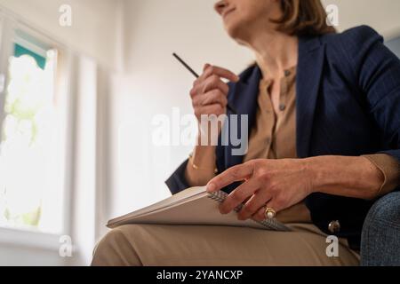 Gros plan d'une femme thérapeute tenant un stylo et un cahier pendant une séance de conseil. L'image véhicule professionnalisme, écoute attentive et préparation. Banque D'Images