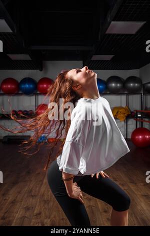 Une femme joyeuse danse librement dans un studio de fitness rempli de balles d'exercice colorées, rayonnant de positivité et d'énergie vers midi Banque D'Images