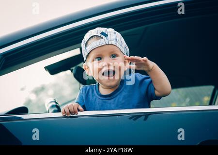 Un petit enfant regarde par la fenêtre de la voiture en riant joyeusement et en agitant sa main Banque D'Images