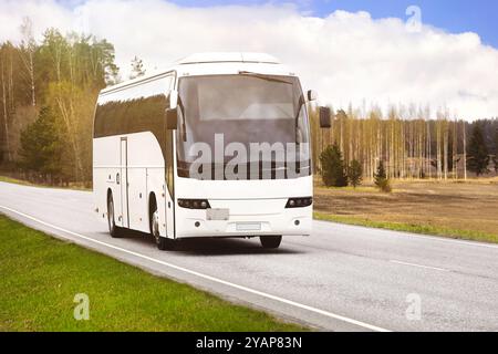 Un autocar blanc transporte des passagers le long de l'autoroute par une belle journée brumeuse du printemps. Banque D'Images