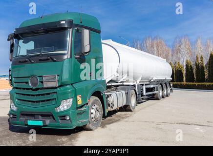 Véhicule utilitaire pour le transport d'affaires. semi-remorque tracteur à cabine verte avec une semi-remorque de réservoir spécialisée debout sur l'asphalte sous un bl Banque D'Images