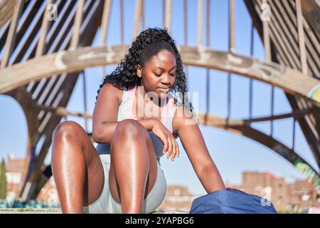 Athlète afro-américaine assise dans un parc se reposant après l'entraînement. Banque D'Images