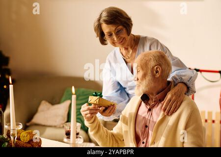 Un couple aîné aimant partage un moment sincère à la maison pendant Noël tout en échangeant des cadeaux. Banque D'Images