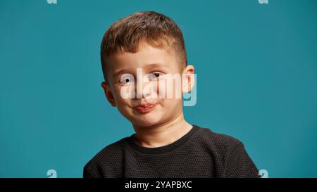 Boy respire le charme ludique et espiègle, avec un léger sourire, l'air qu'il essaie de retenir R secret sur fond bleu de studio. Banque D'Images