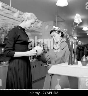 Shopping dans les années 1950 Une jeune femme dans un magasin où une vendeuse présente une sélection de magasins de céramiques fines et d'objets décoratifs conçus par le célèbre designer Stig Lindberg. Elle est vue tenant un vase dans ses mains le montrant correctement pour la cliente féminine. 1956 Conard ref 3181 Banque D'Images