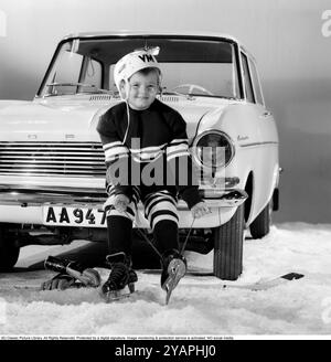 Hockey sur glace dans les années 1960 Un garçon est assis à l'avant d'une voiture Opel Kadett mettant ses patins dans son équipement de hockey sur glace. Il est prêt à jouer au hockey sur glace. 1963. Kristoffersson ref DE1-10 Banque D'Images