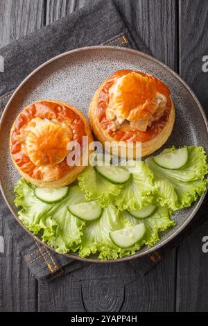 Bouchee a la reine ou vol-au-vent avec veau en sauce épicée servi avec laitue et concombre gros plan dans une assiette sur une table en bois. Vue verticale de dessus f Banque D'Images