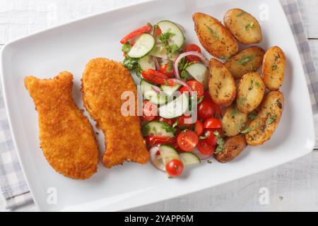 Poisson pané frais croustillant avec pommes de terre et salade de légumes frais gros plan dans une assiette sur une table en bois. Vue horizontale de dessus Banque D'Images
