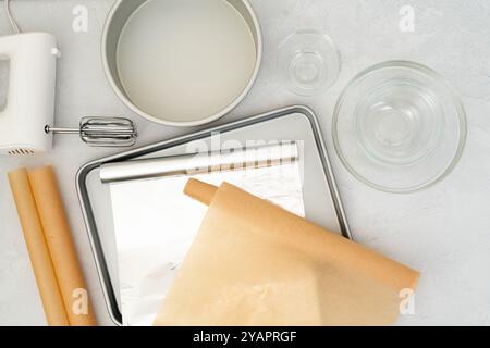 Composition à poser à plat comprenant du papier parchemin, une feuille d'aluminium, un moule à pâtisserie, un mélangeur et des bols en verre disposés en vue rapprochée sur un dos gris clair Banque D'Images