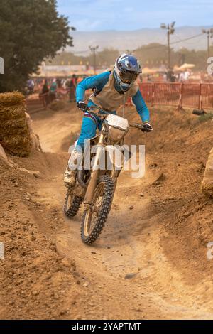 Pilote de motocross en action se préparant à prendre un virage serré sur un terrain poussiéreux lors d'une compétition d'endurance en plein air Banque D'Images