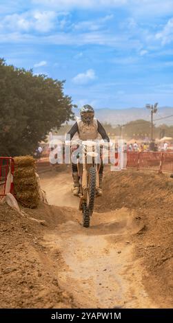 Un pilote de motocross saute et roule son vélo sur un changement de colline sur une piste de terre lors d'une course d'endurance de motocross avec des spectateurs derrière la protection f Banque D'Images