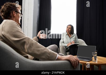 Un journaliste s’engage dans une interview réfléchie avec un spécialiste, prenant des notes et sirotant de l’eau. Banque D'Images