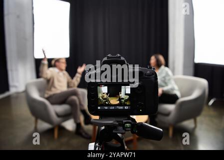 Un journaliste d’âge moyen s’engage dans un entretien professionnel avec un spécialiste dans un environnement de studio contemporain. Banque D'Images