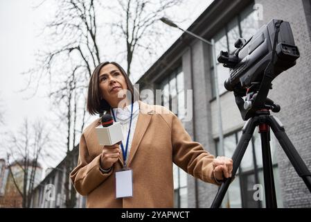 Une femme journaliste se tient confiante avec un micro à la main, prête à diffuser des nouvelles à l'extérieur. Banque D'Images